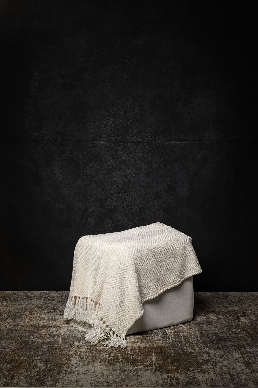 The Studio Smoke backdrop behind a white seat draped with a cream throw: hand-painted charcoal canvas, deep and mottled.