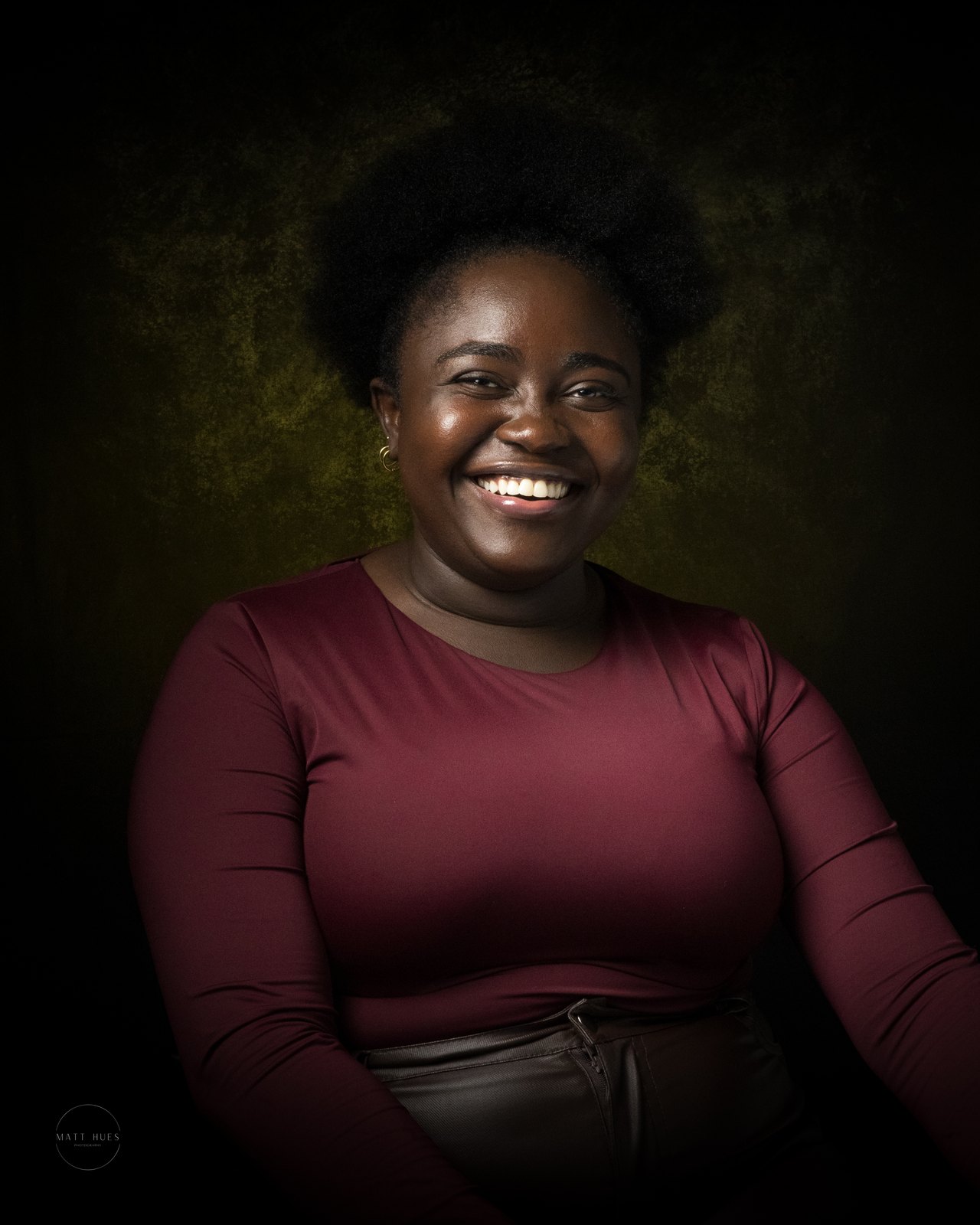 A woman in maroon laughs on a green-to-black backdrop, warm light across her face.