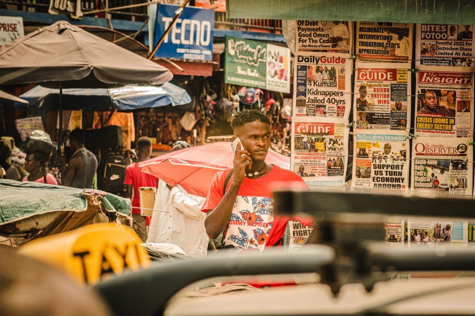 A man takes a call at a newspaper stand in Ghana, front pages strung behind him.