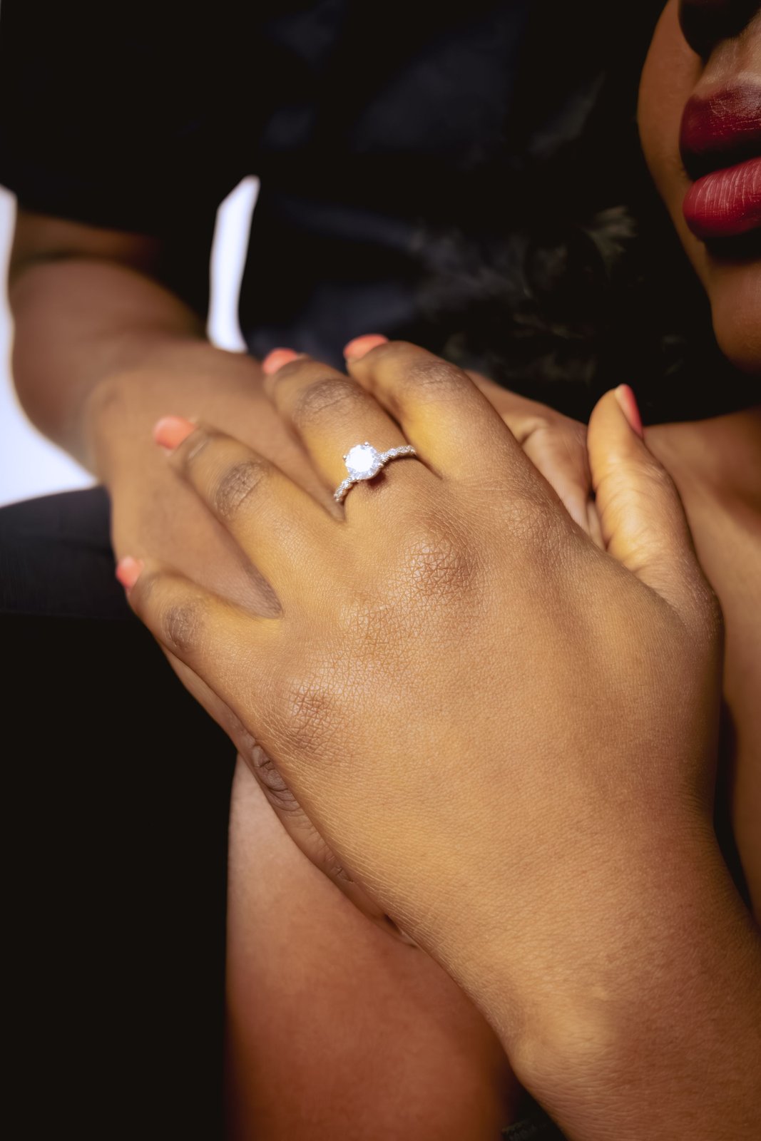 A close frame of her hands crossed at her chest, the engagement ring catching the light.